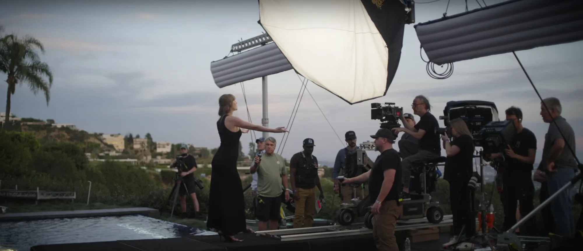 Taylor Swift directing her 'Patient Zero' music video, surrounded by crew and equipment on set outdoors.