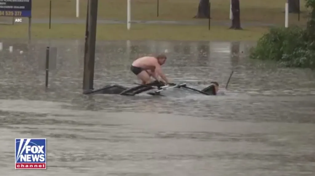 A TV reporter and a bystander rescue a man trapped in a sinking vehicle during rising floodwaters.