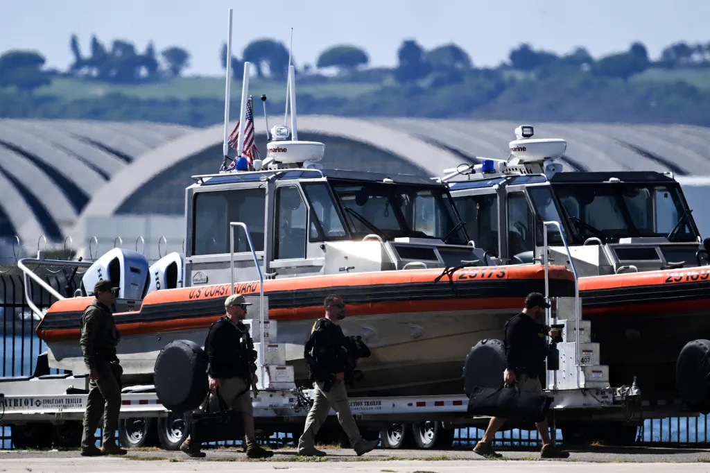 U.S. Coast Guard personnel walk in front of response boats on trailers.