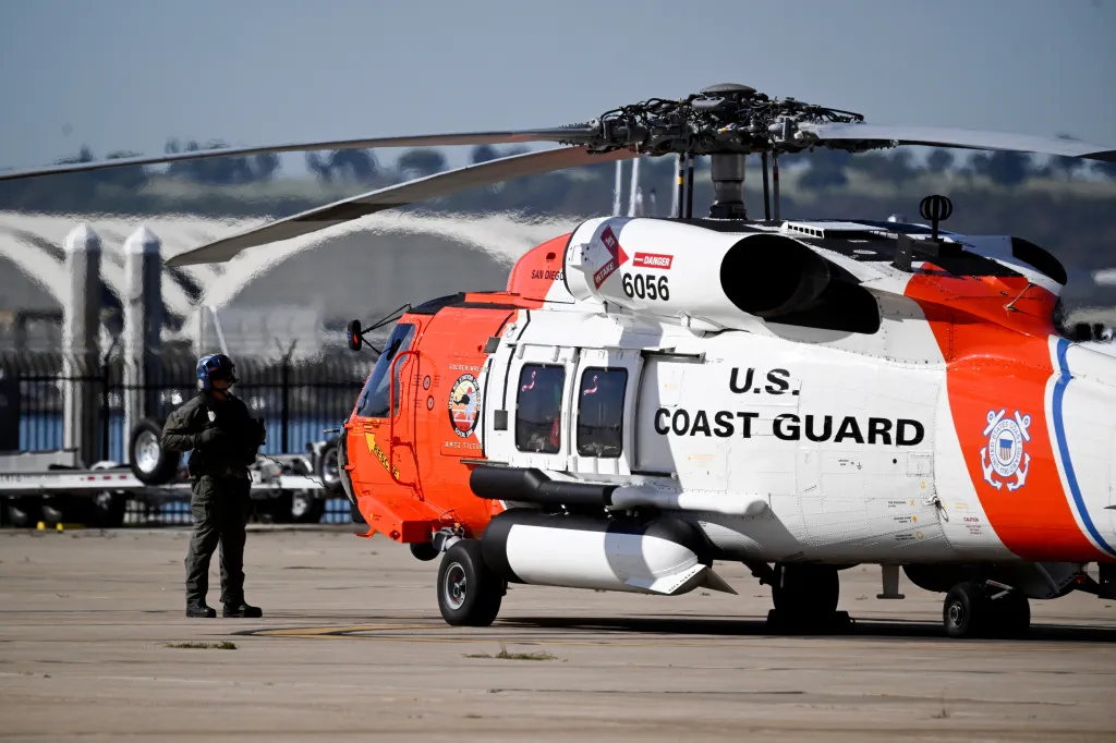 A U.S. Coast Guard crew member stands near a helicopter preparing for liftoff at Coast Guard Station San Diego.