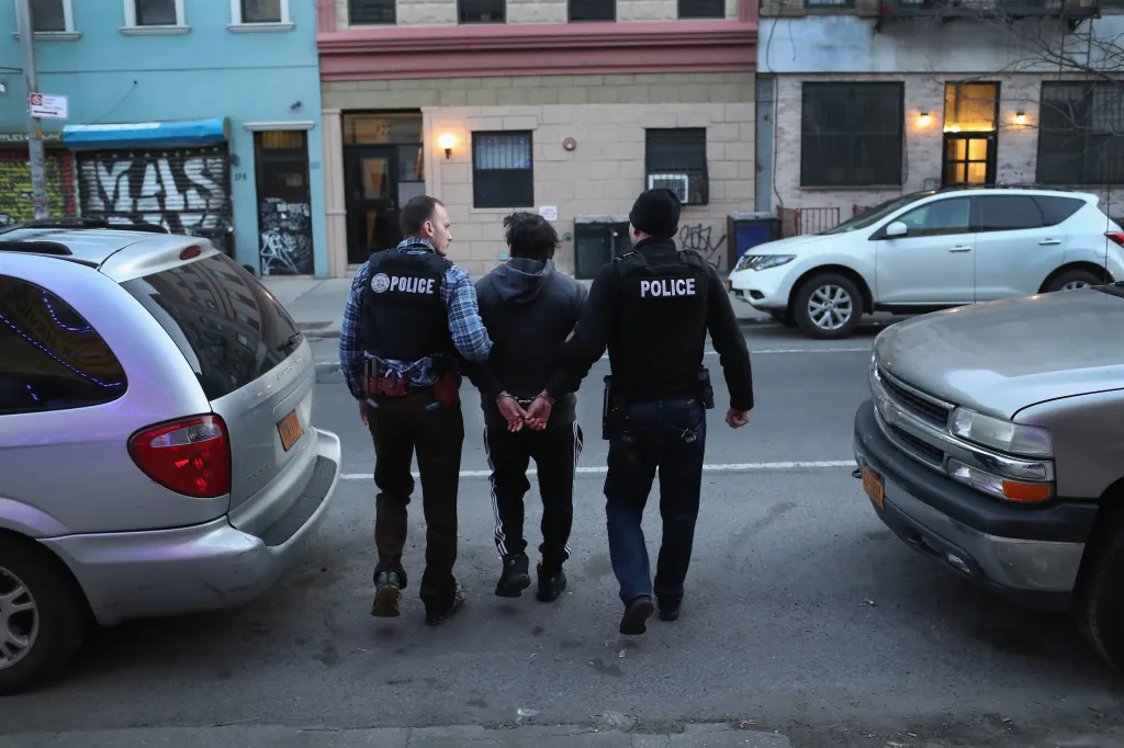 U.S. Immigration and Customs Enforcement officers lead a handcuffed man down a New York City street during an operation.