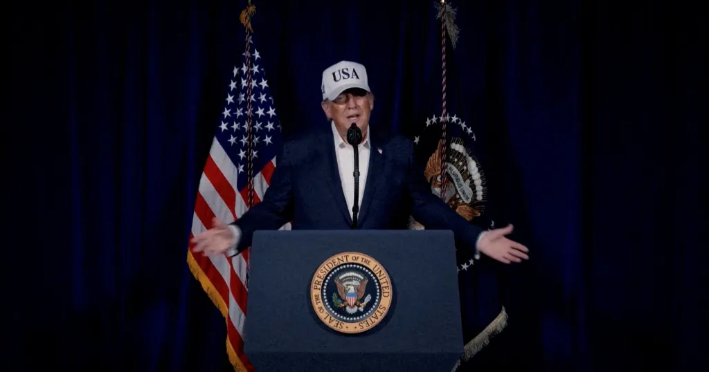 U.S. President Donald Trump speaks at a podium with American and presidential flags in the background.