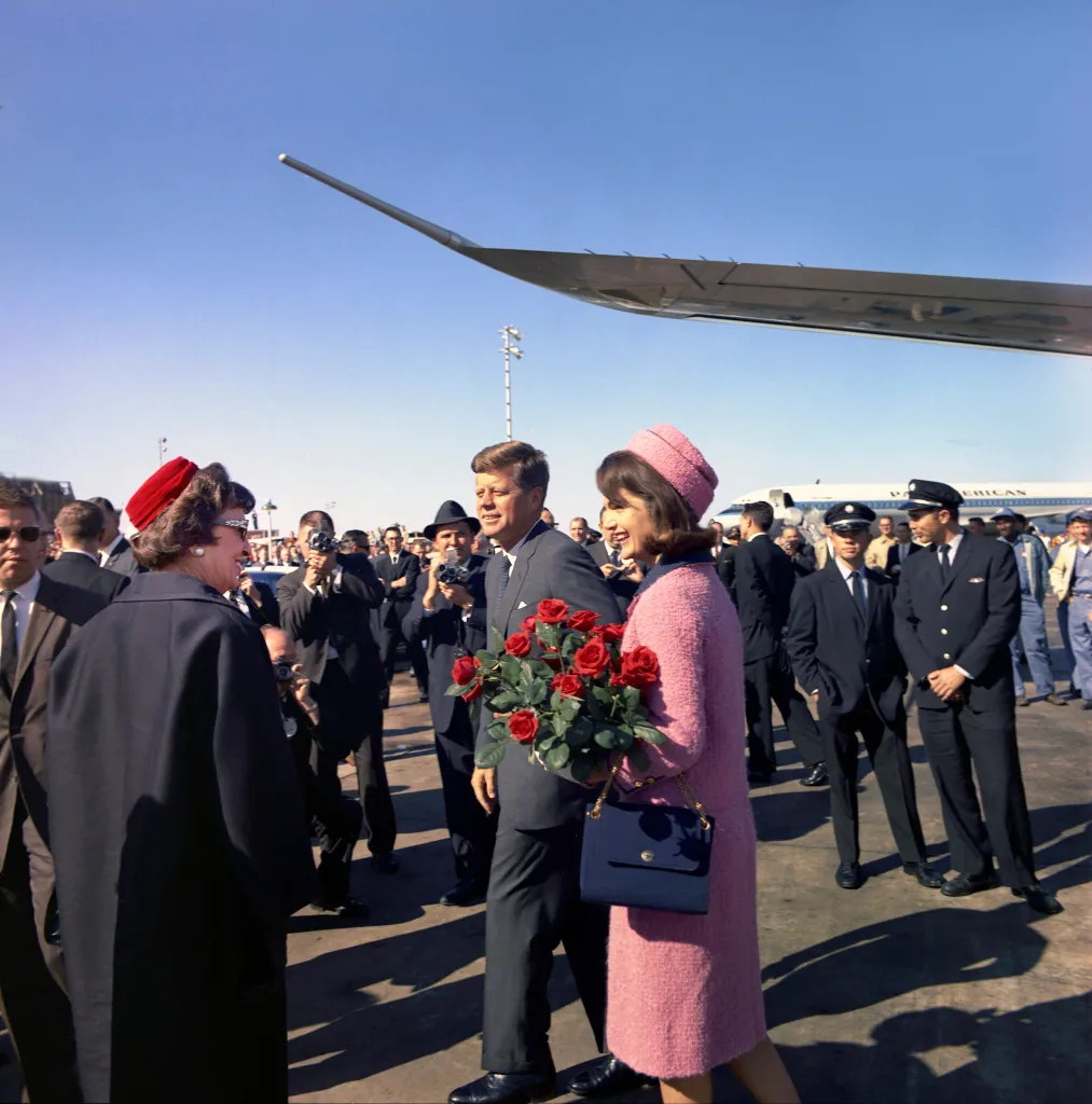 President John F. Kennedy and First Lady Jacqueline Kennedy arrive at Love Field in Dallas, Texas, with Mrs. Kennedy holding a bouquet of red roses.