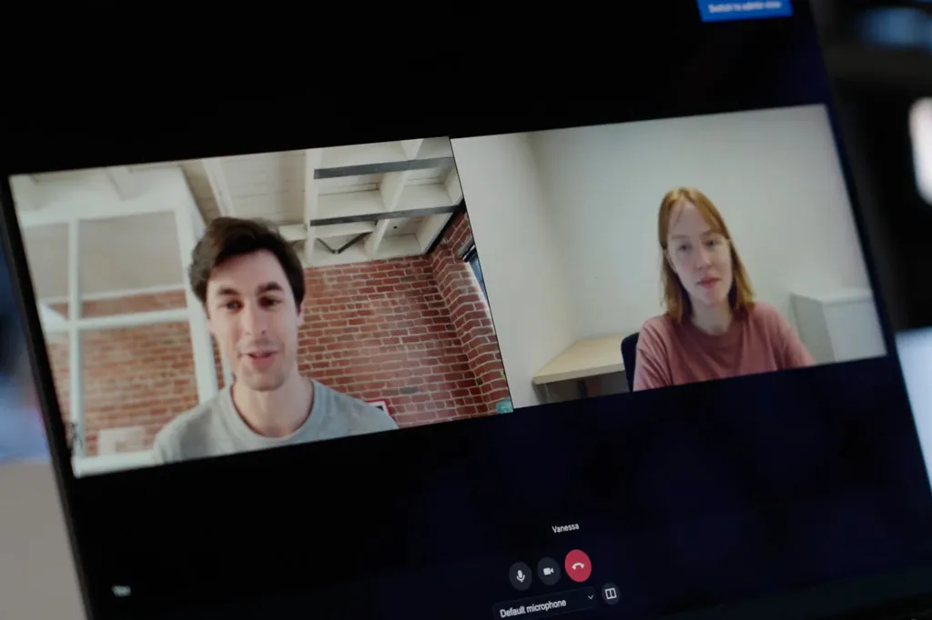 A laptop screen displays a video call between a man in an office and a woman labeled 