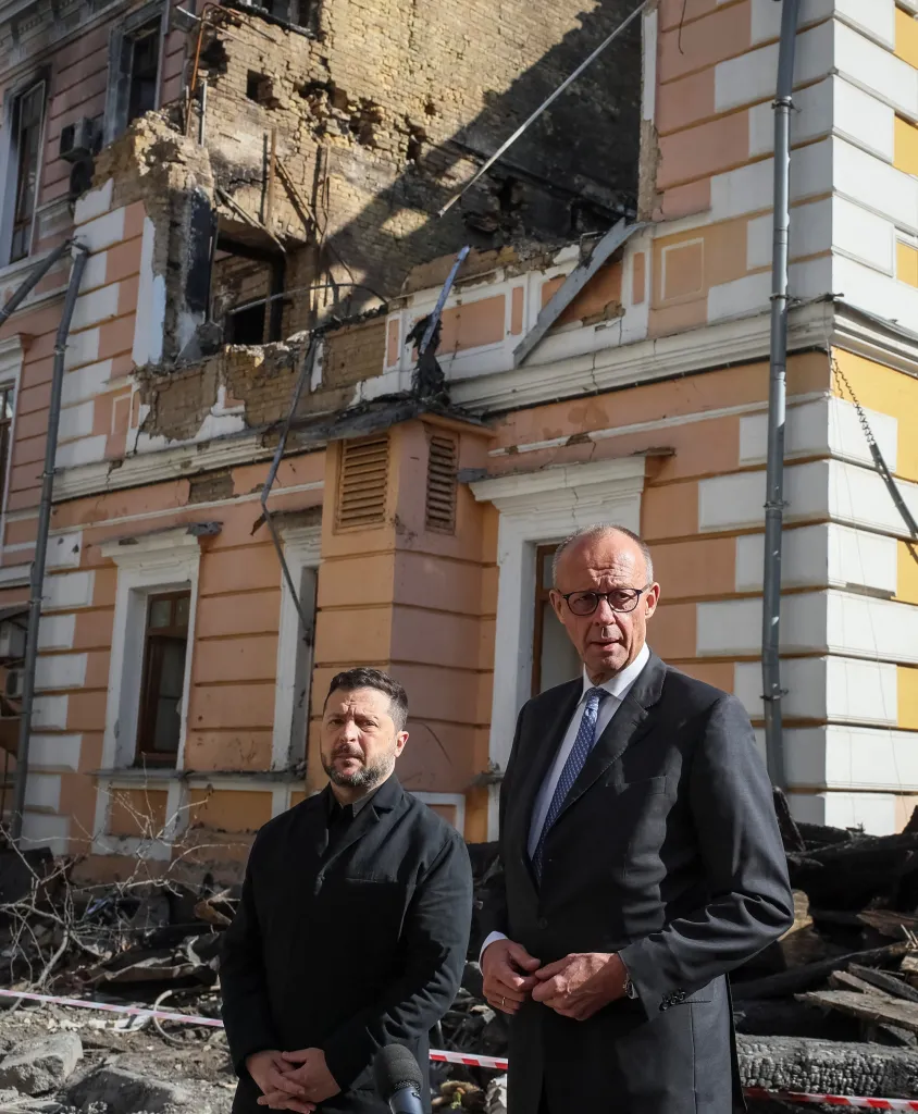 Ukrainian President Volodymyr Zelenskiy and German Chancellor Friedrich Merz stand before a damaged building in Kyiv.