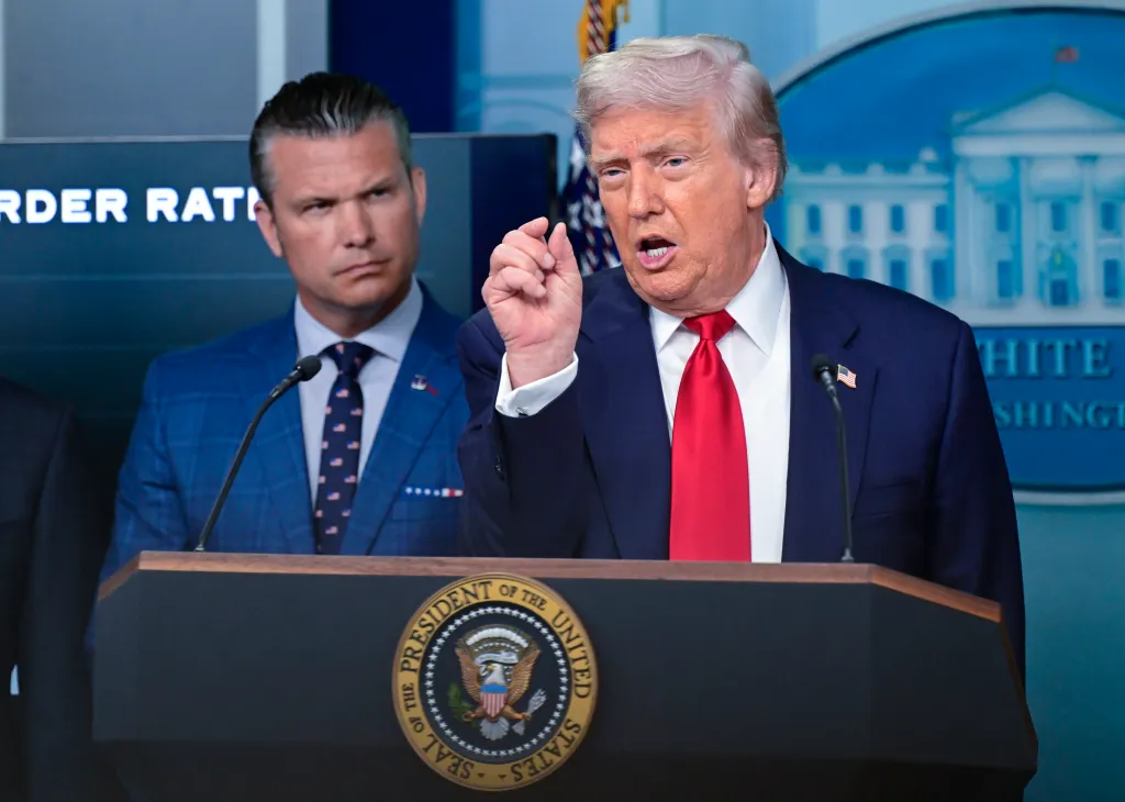United States President Donald J. Trump gestures during a press conference at the White House, with United States Secretary of Defense Pete Hegseth looking on from behind.