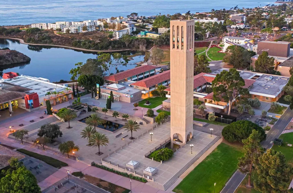 An aerial view of the University of Santa Barbara campus, featuring the Storke Tower and surrounding buildings with the ocean in the background.