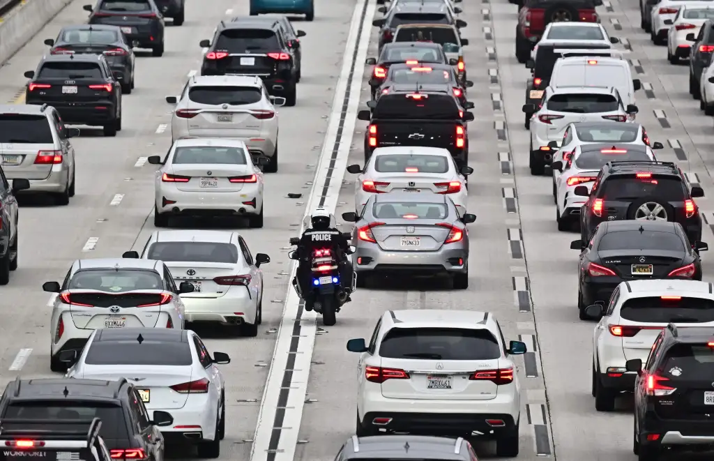A police motorcycle officer weaves through heavy traffic on a Los Angeles freeway.