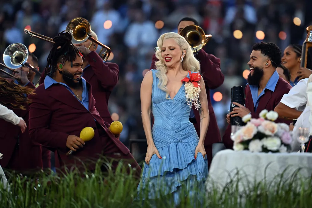 Lady Gaga performs in a light blue dress with musicians and trombonists.