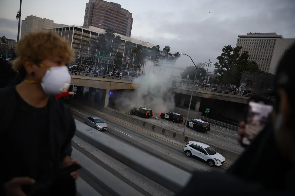 Smoke rises from California Highway Patrol vehicles damaged by vandals throwing rocks and debris from an overpass during a protest in Los Angeles.