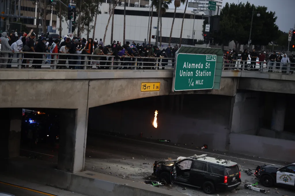 Protesters gather on an overpass, throwing rocks and debris down at California Highway Patrol vehicles parked below during a protest.