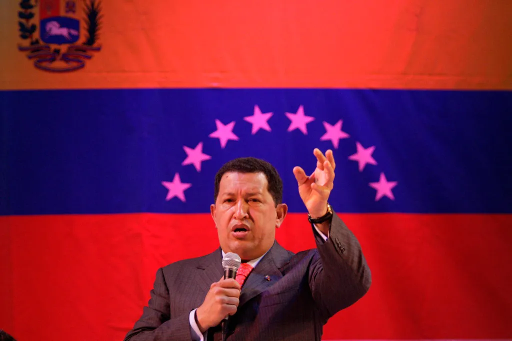Venezuelan President Hugo Chavez addresses an audience with a microphone in front of the Venezuelan flag.