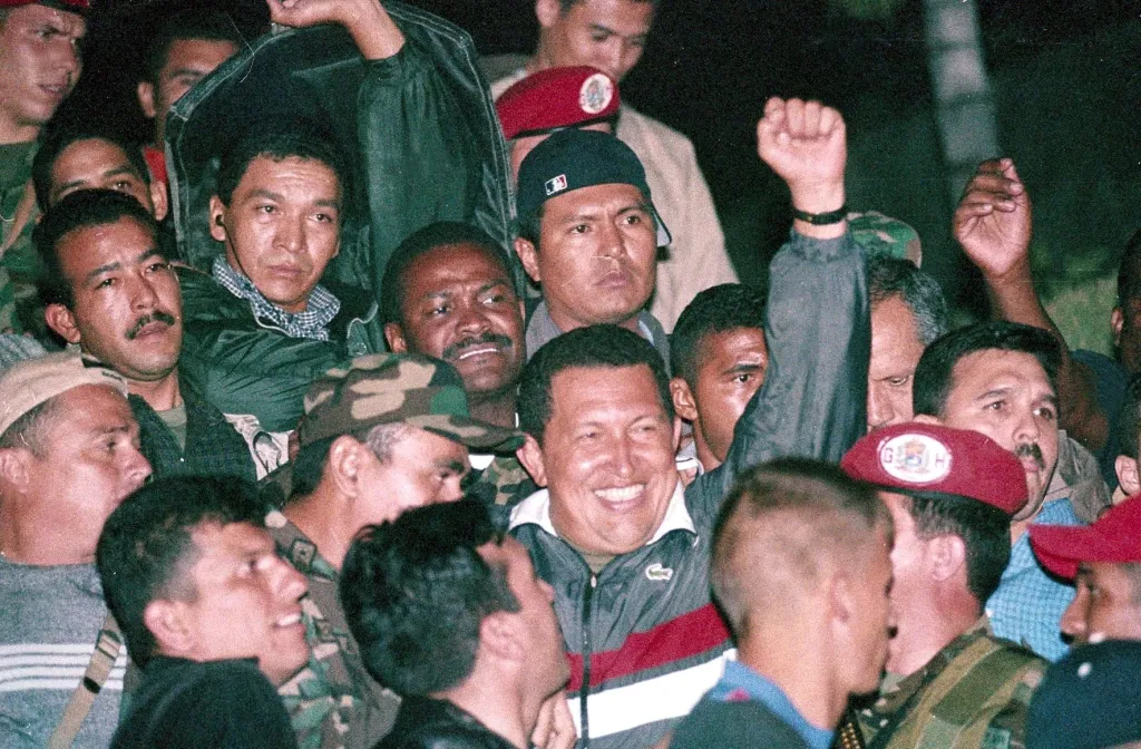 Venezuelan President Hugo Chavez smiles and raises his fist in celebration while surrounded by a cheering crowd upon his return to office.