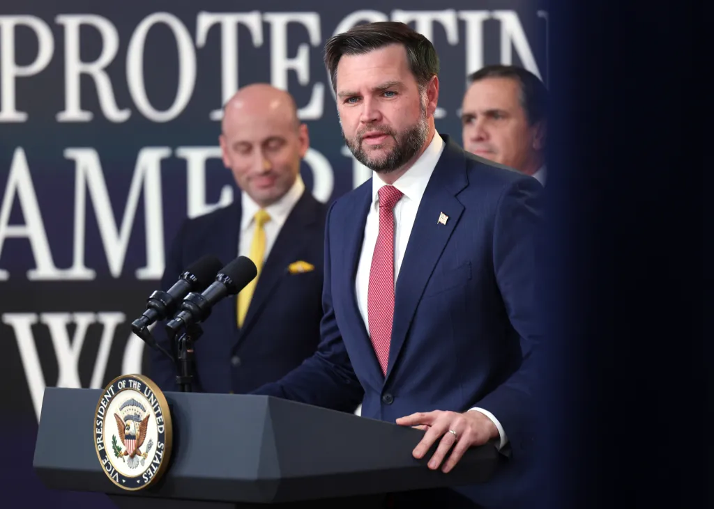 Vice President JD Vance speaks at a news conference behind a podium bearing the seal of the Vice President of the United States.