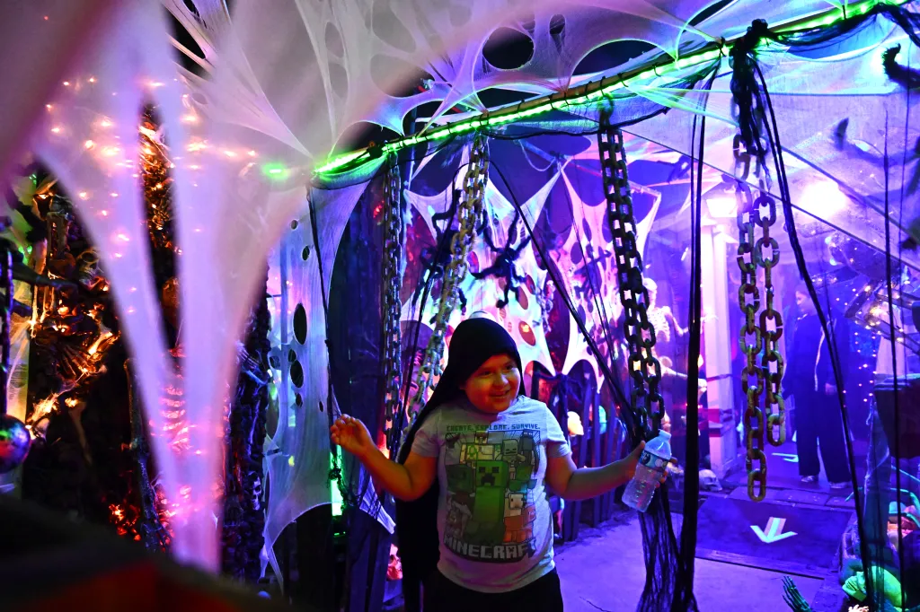 A young visitor walks through a maze inside the Buena Vista Haunt, decorated with spider webs, chains, and green and purple lighting.