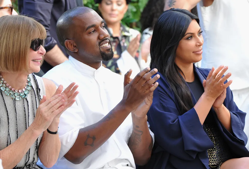 Anna Wintour, Kanye West, and Kim Kardashian clap at an event.