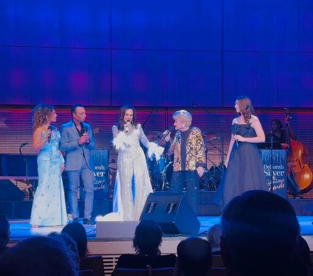 Deborah Silver and fellow performers singing on stage during the