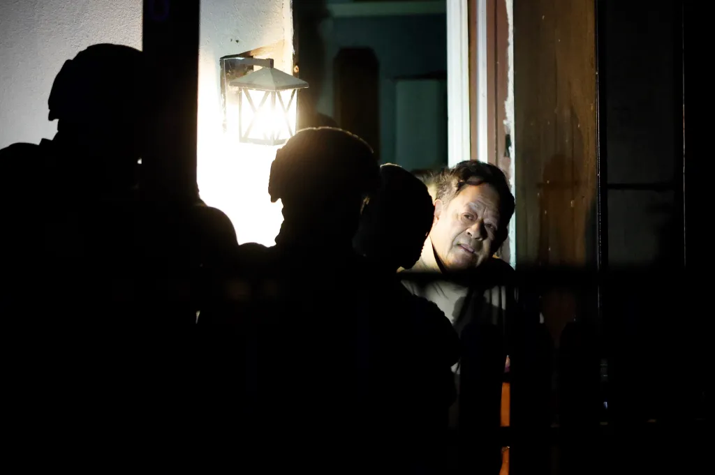 A man stands in an open doorway while law enforcement officers in silhouette stand in the foreground during a raid in Los Angeles.