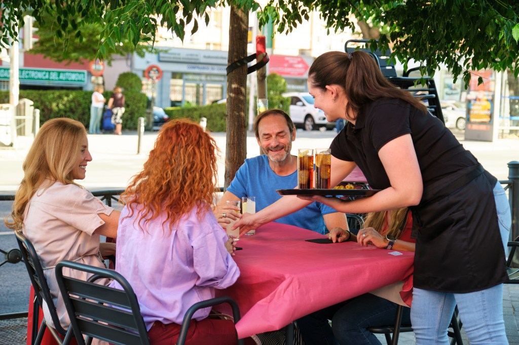 Waitress serving drinks and olives to a group of mature friends at a restaurant table.