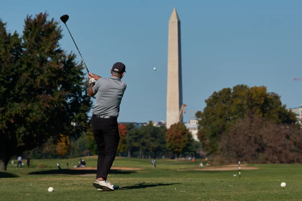 A golfer takes a swing at East Potomac Park Golf Course with the Washington Monument in the background.