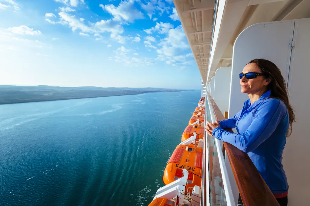 A woman standing on a ship's cabin balcony, looking out over the water in the Suez Canal.