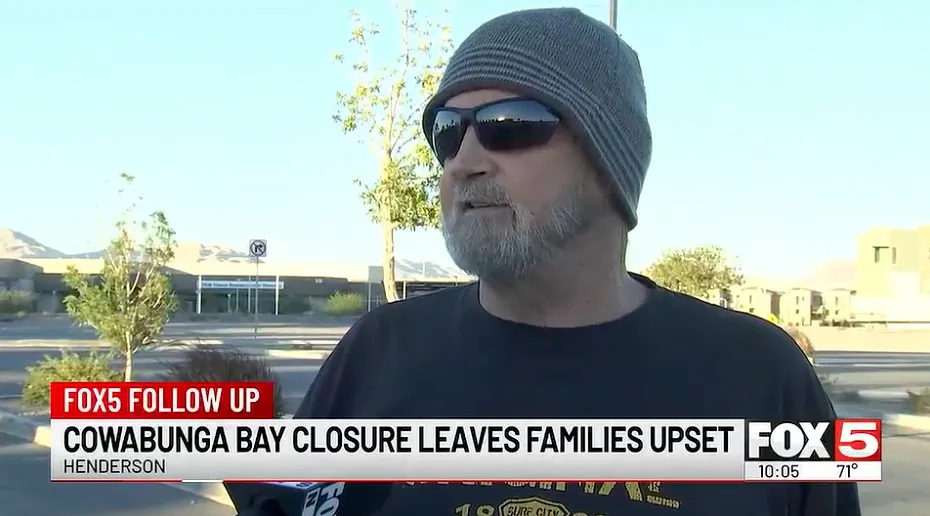 A man in a gray beanie and sunglasses being interviewed outside in front of a building.