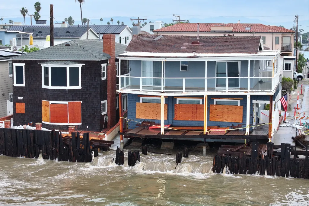 Waves crash into homes with boarded-up windows in Long Beach, California.
