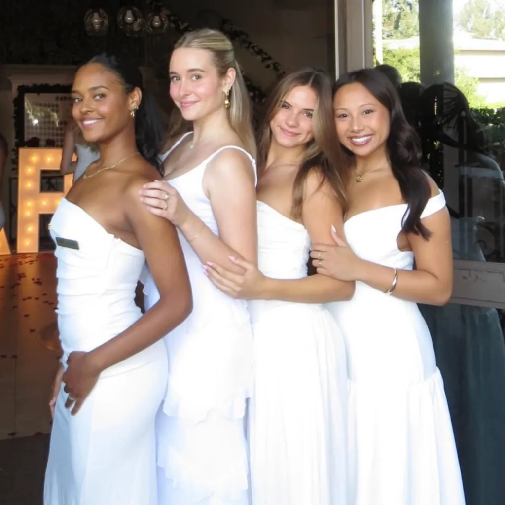 Sky Achola, standing on the far left, poses with three other women in white dresses.