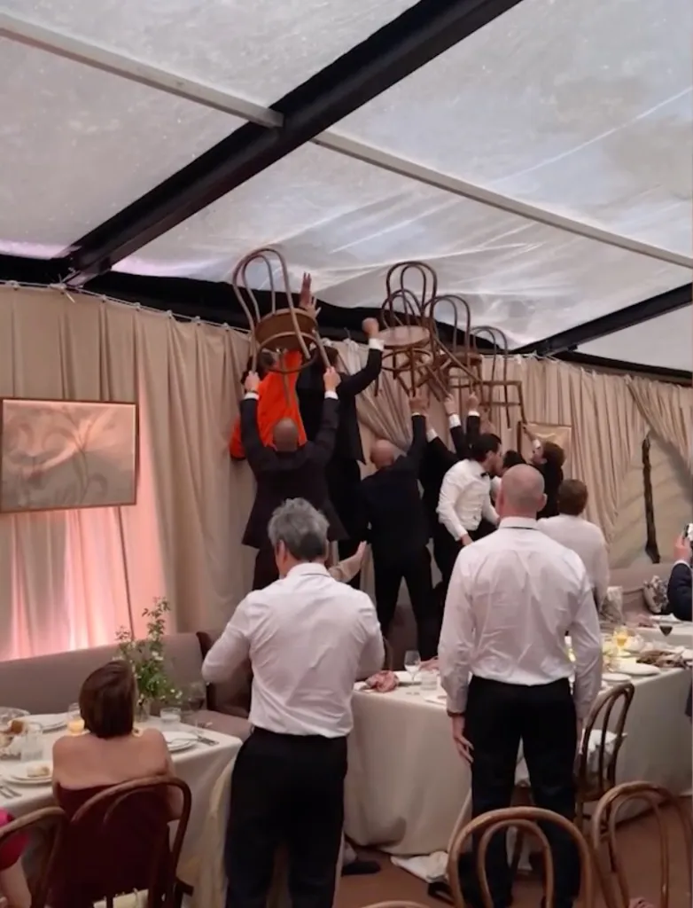 Wedding guests using chairs to prevent rainwater from sagging a venue's canopy.