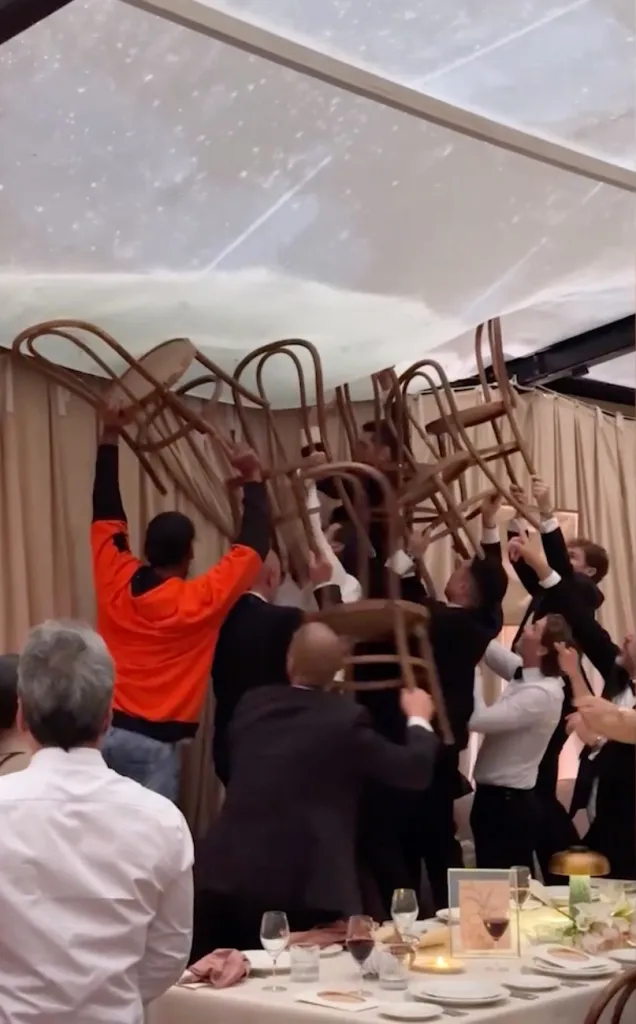 Wedding guests use chairs to hold up a sagging tent ceiling filled with rainwater to prevent flooding.
