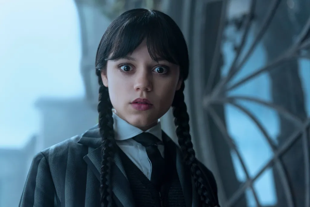 Jenna Ortega as Wednesday Addams looking shocked, with her dark hair in braided pigtails.