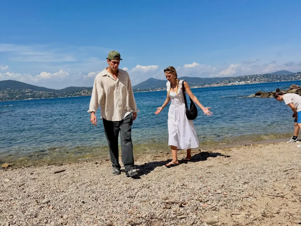Cast members of The White Lotus walking on a beach by the sea.