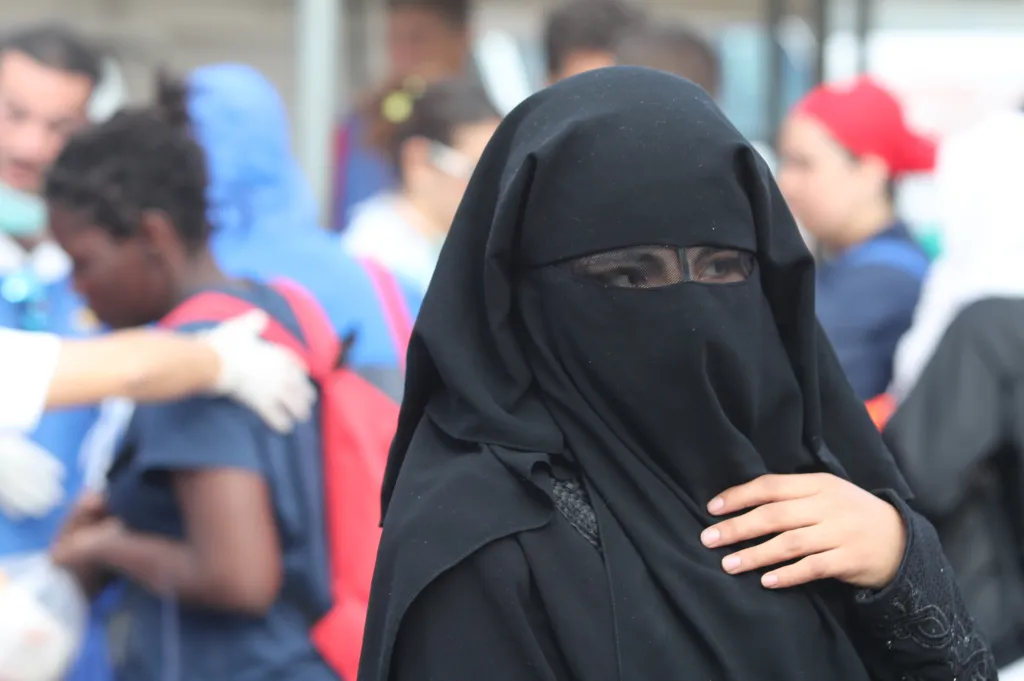 A woman wearing a black burqa amidst a crowd of migrants.