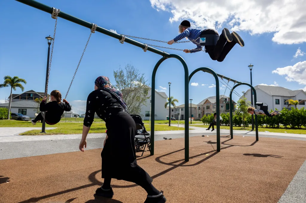 A woman pushes children on a swing set at a playground