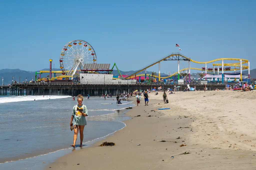 A woman reads a book as she walks on the beach near the Santa Monica Pier.