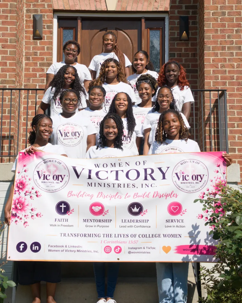 Photo of members of Women of Victory Ministries holding a banner in front of a brick building.