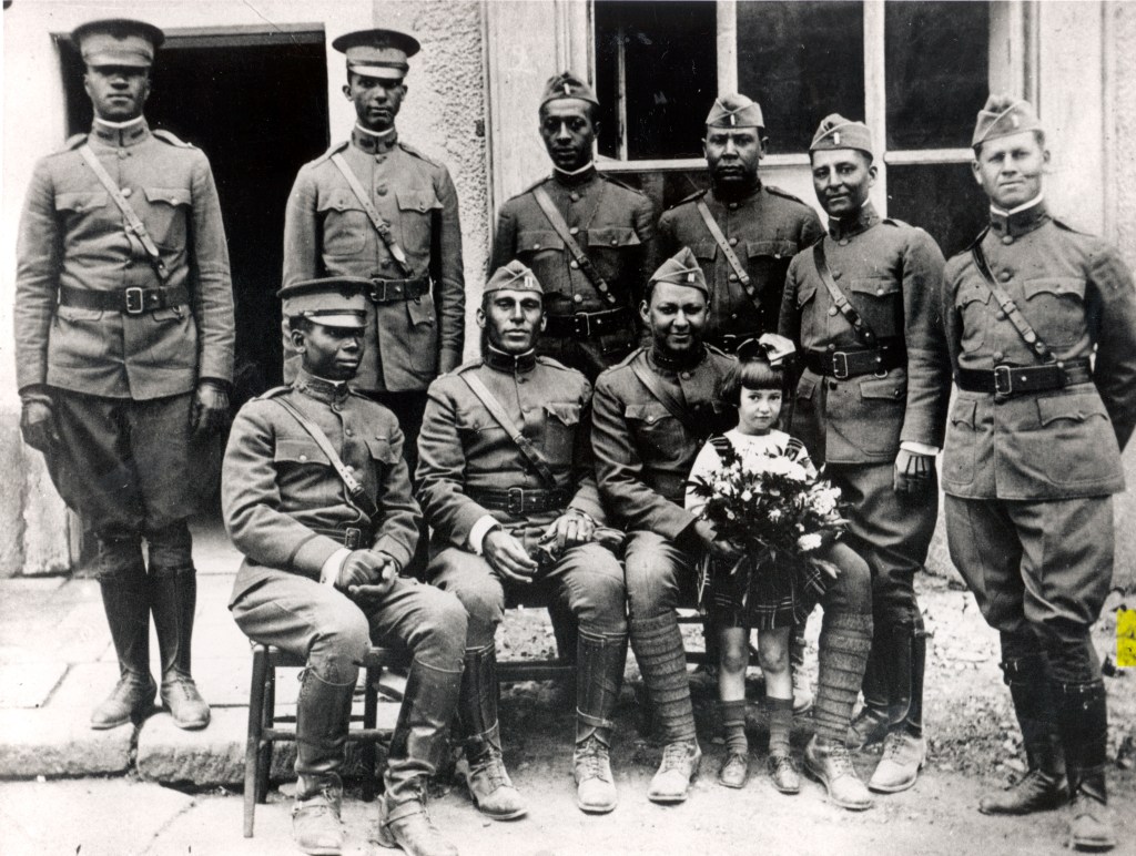 African-American officers of the Buffalo Soldiers pose for a group photo during World War I, with a young girl holding flowers standing among them.