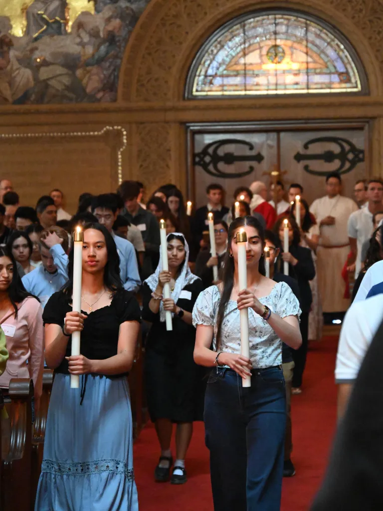 Students holding lit candles while walking down the aisle of a church.