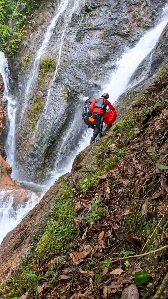 Rescuers navigate a steep, rocky cliff next to a waterfall.