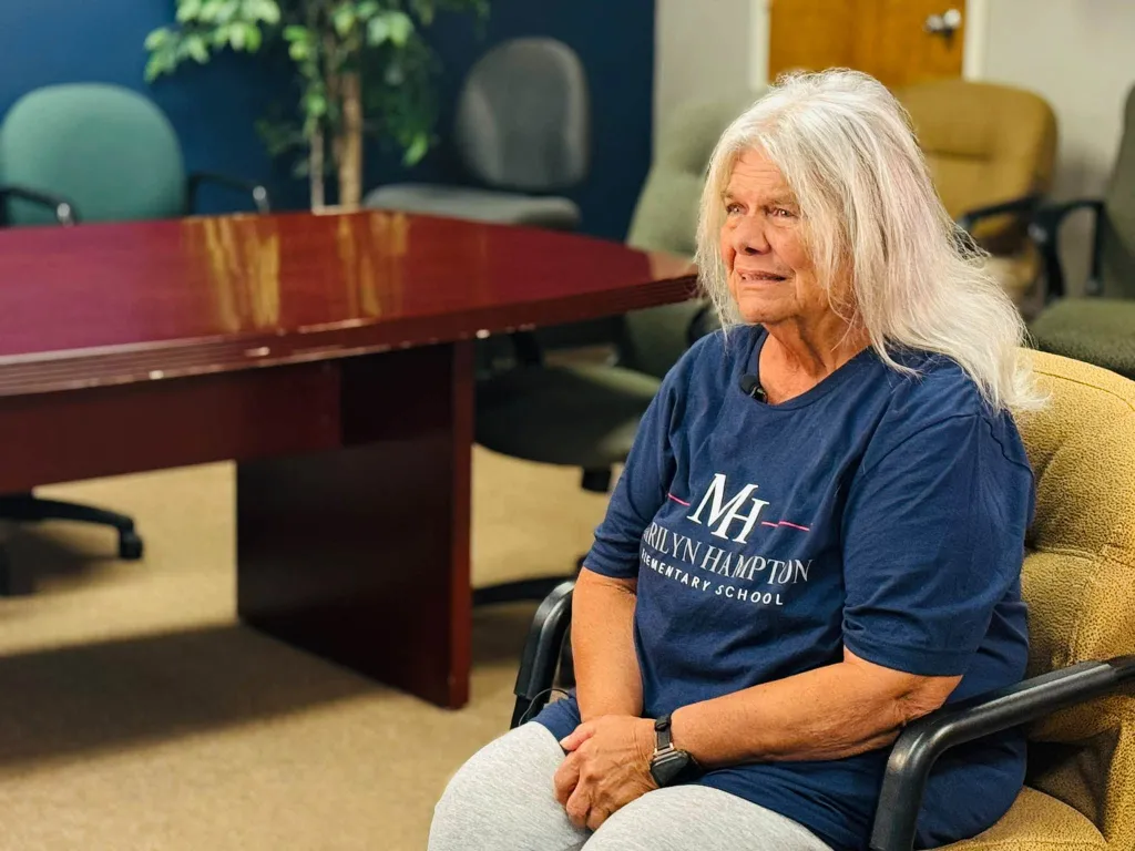 Marilyn Hampton, a retired custodian, smiling in an office with a conference table in the background.