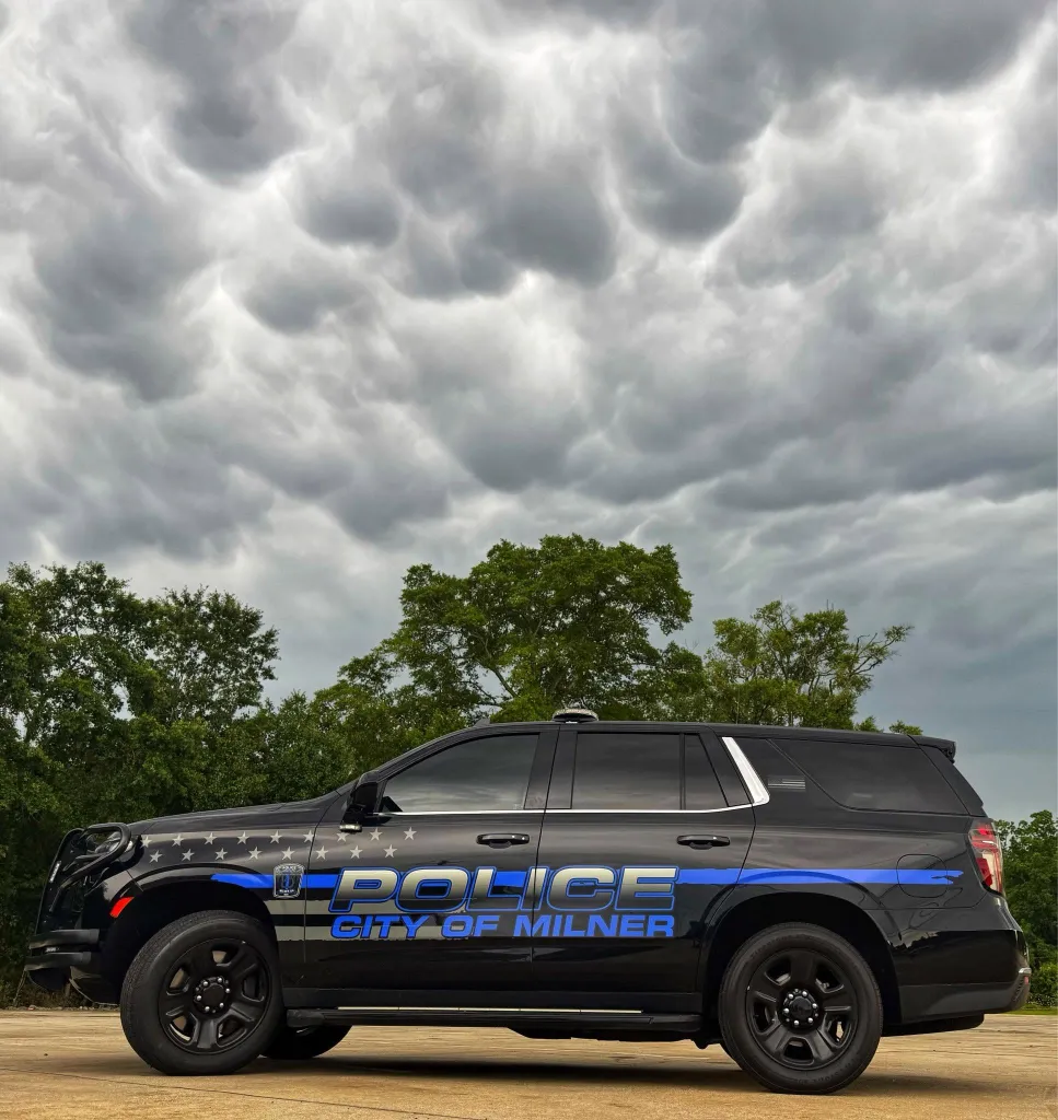 A black City of Milner police vehicle parked outside under a cloudy sky.