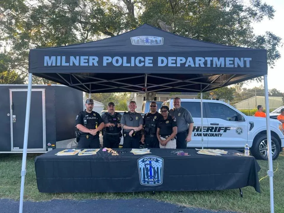 Six police officers stand behind a table with informational items under a Milner Police Department tent.