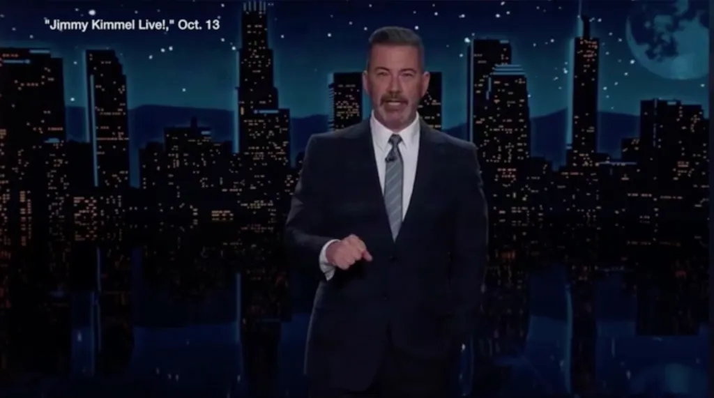 Jimmy Kimmel on his talk show set in front of a city skyline backdrop.