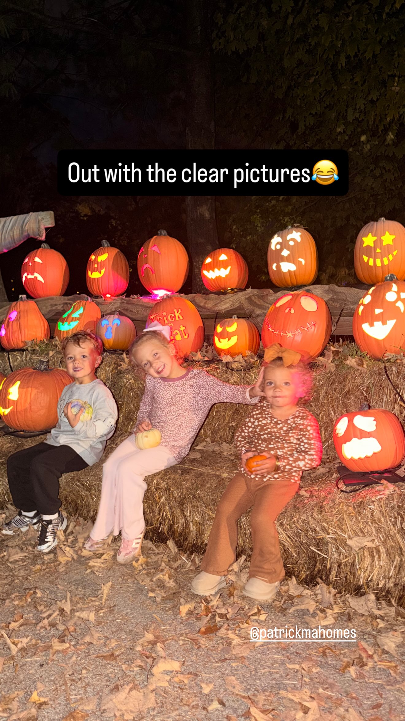 Patrick and Brittany Mahomes' three children sitting on a hay bale in front of lit jack-o'-lanterns.