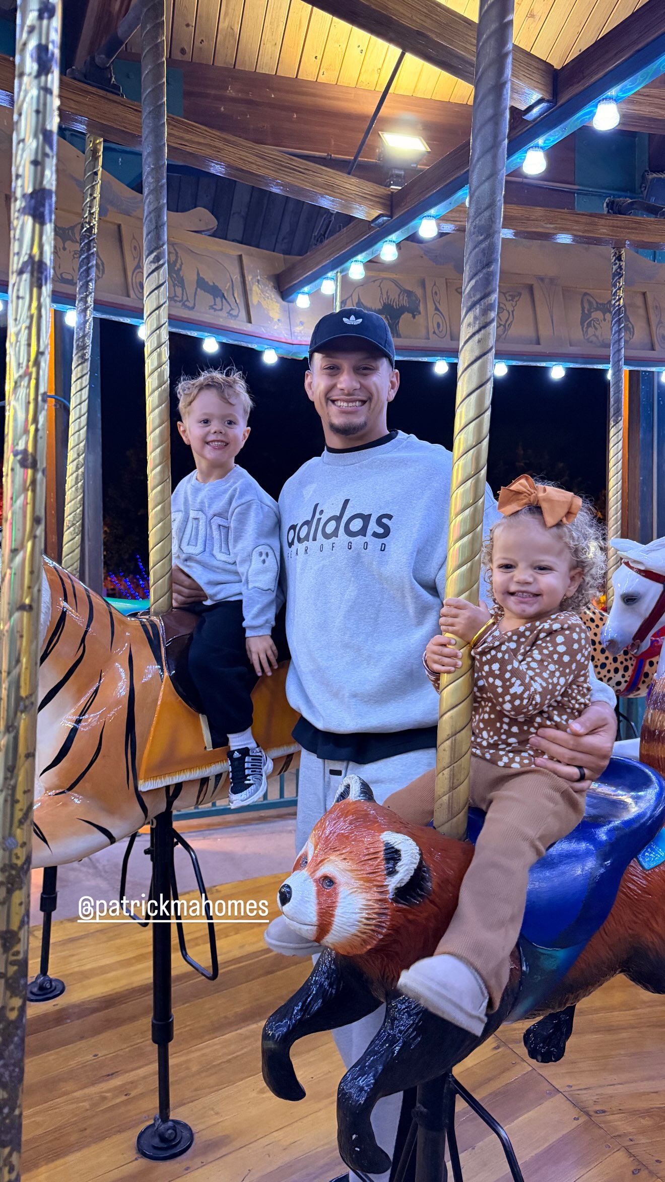 Patrick Mahomes smiles on a carousel with his son sitting on a tiger and his daughter riding a red panda.