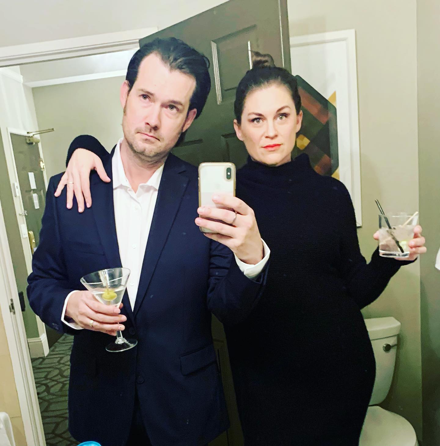 David Bowick and a woman taking a bathroom selfie while holding drinks.