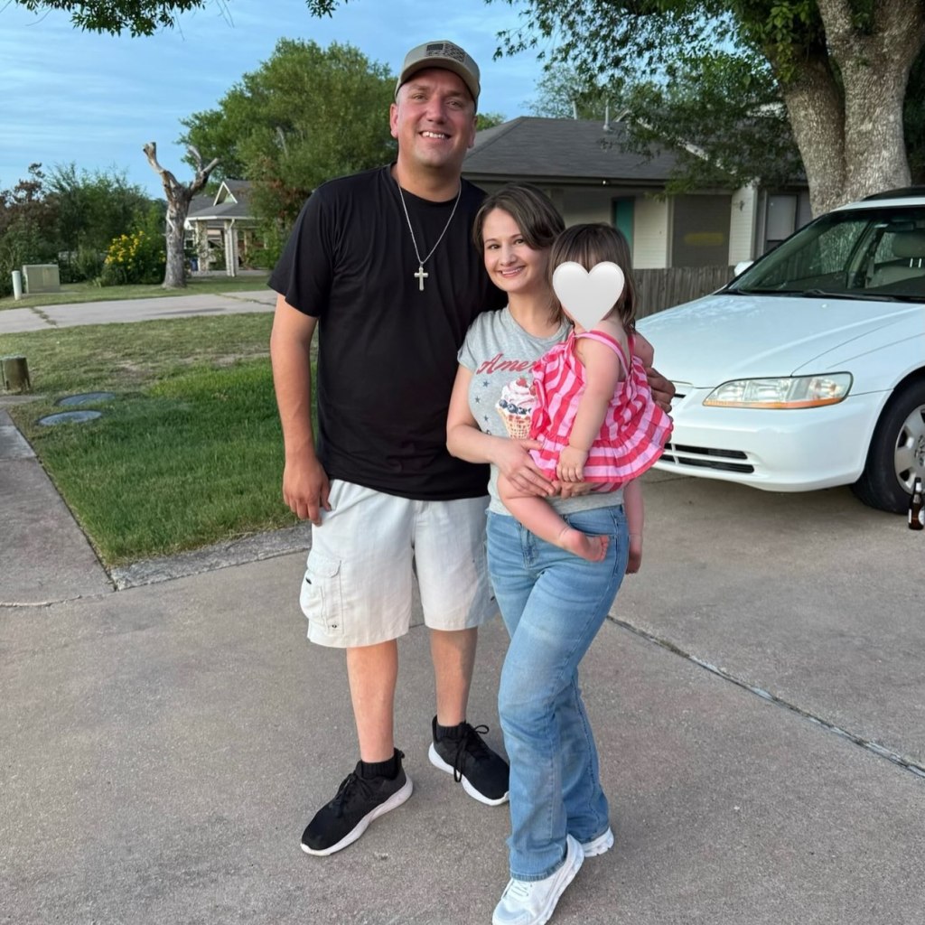 Gypsy Rose Blanchard and Ken Urker posing outdoors with a toddler, whose face is covered by a white heart.