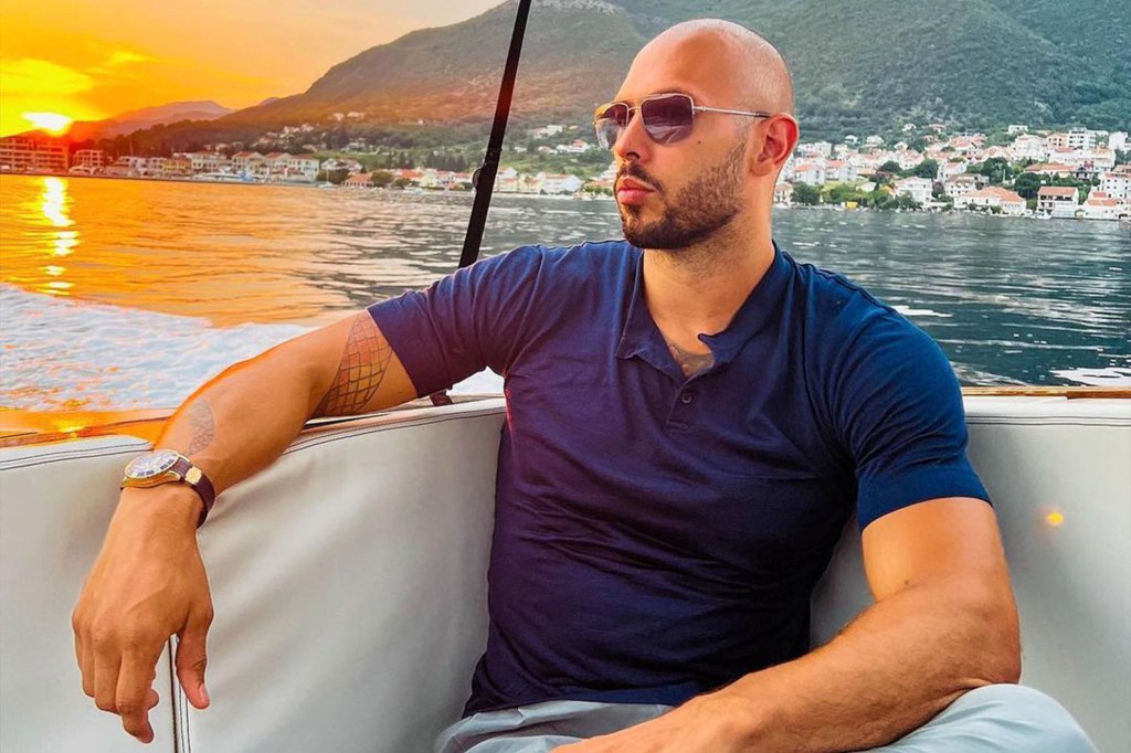 Andrew Tate wearing sunglasses on a boat at sunset.