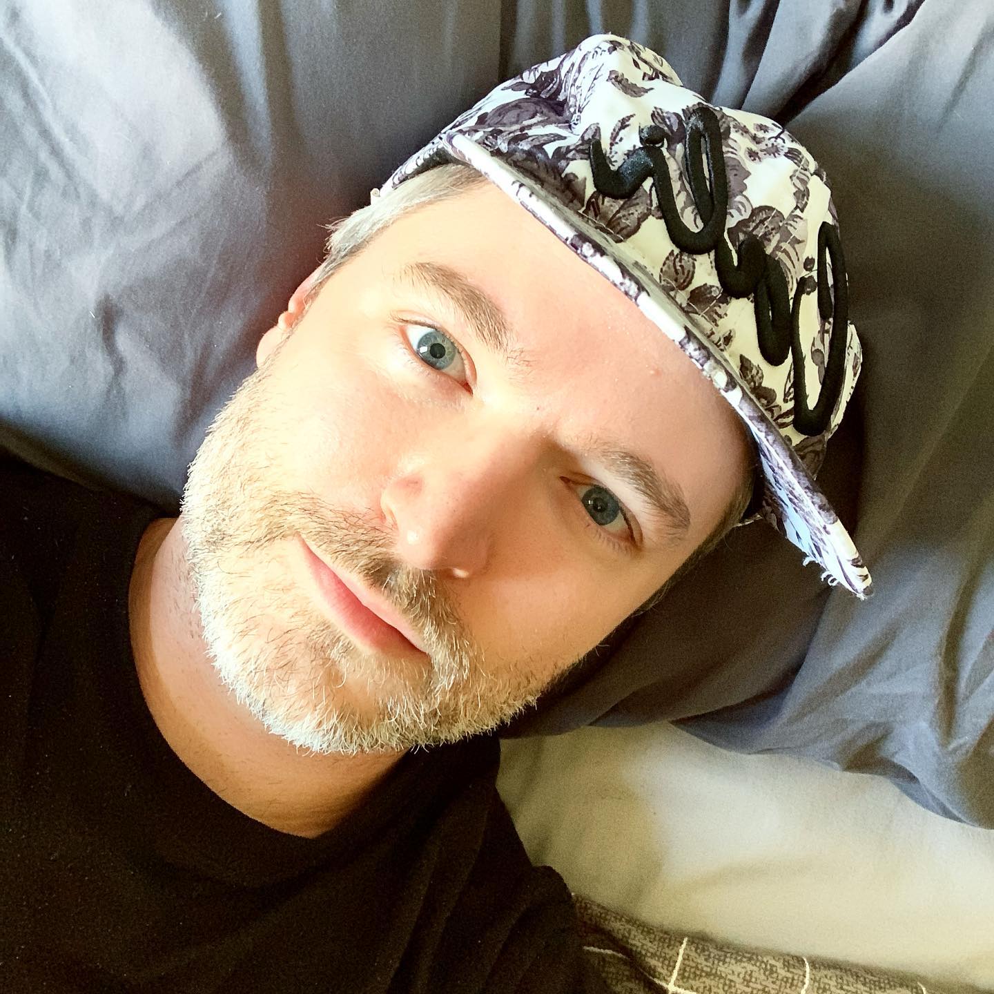 Lucian Piane lying down, wearing a patterned cap and a black shirt.