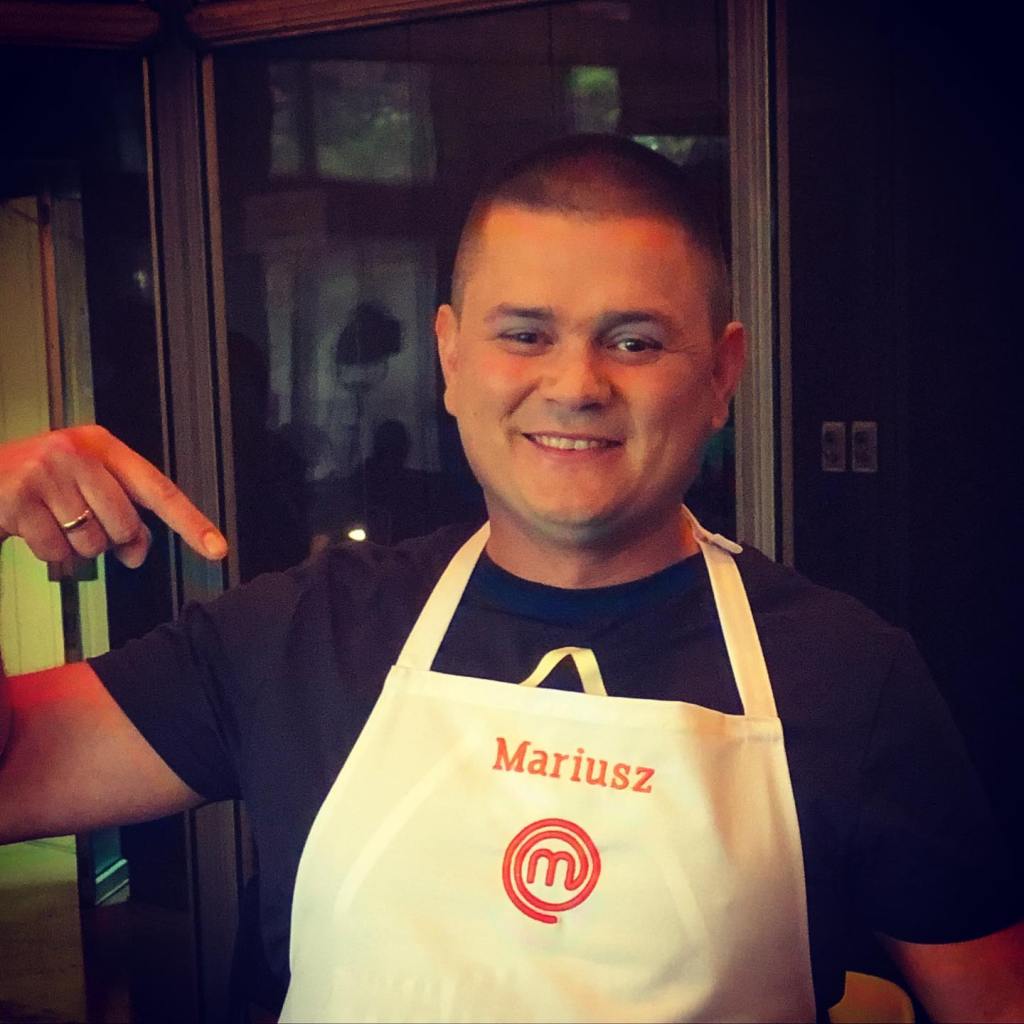 Polish 'MasterChef' star Mariusz smiling while wearing a white apron.
